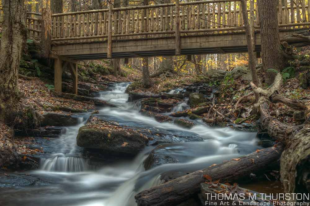 A flowing stream under a wooden footbridge splits between a large rock at Bushkill Falls, Pennsylvania.