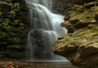 A wispy, soft textured waterfall at Bushkill Falls, Pennsylvania flows off jagged rocks into the water below on an Autumn overcast day.